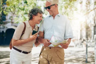 Elderly man and woman laughing. The man is holding a map, and the woman is wearing a backpack. They look like they are travelling.